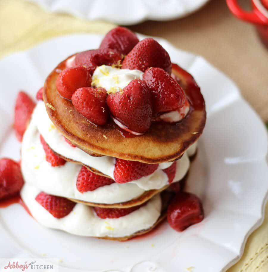 An overhead photo of a stack of strawberry cheesecake protein pancakes with berries on top.