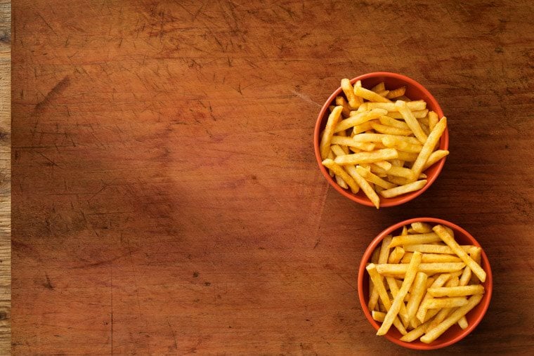 Two red ramekins filled with french fries on a wooden background