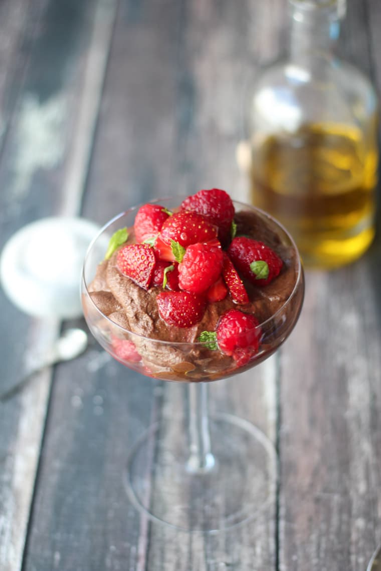 close up of vegan chocolate and olive oil mousse topped with macerated berries in a clear dish