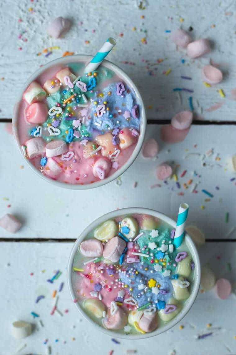 An overhead image of two mugs of unicorn hot chocolate, pastel coloured toppings and straws.