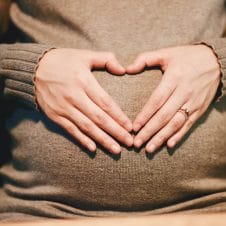 Hand making a heart over a pregnant stomach.