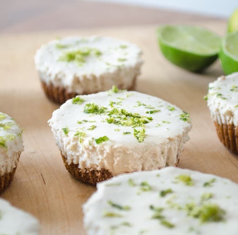 close up shot of vegan mini key lime pies garnished with lime zest on a wooden serving platter