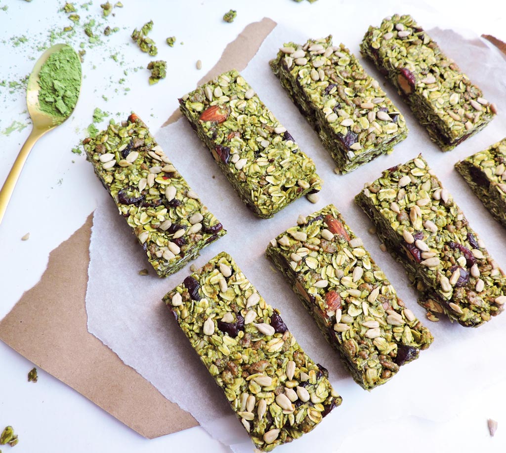 birds eye view of seven no bake green super matcha bars served on parchment paper next to a spoonful of matcha powder