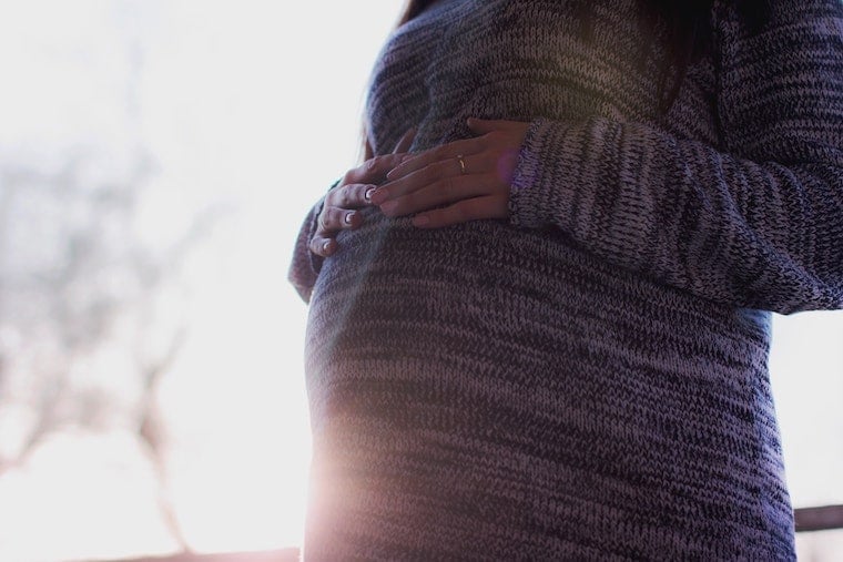 A woman holding her pregnancy bump referring to the question "Can you diet while pregnant?".