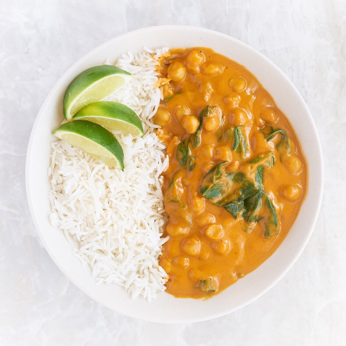 Bowl of white rice and curry with lime wedges.