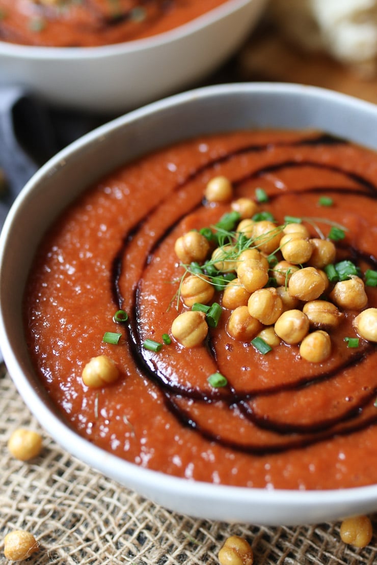 Roasted tomato and fennel soup in a white bowl garnished with chickpeas, herbs, and balsamic.