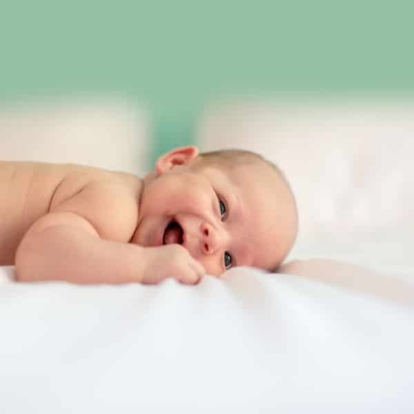 Happy baby lying on a white blanket.