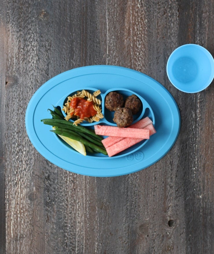 Baby led weaning dinner on a blue plate containing pasta with tomato sauce, meatballs, green beans and watermelon. 