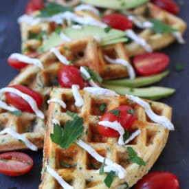 Egg and cheese savoury protein waffles topped with sliced avocados, cherry tomatoes, creamy drizzle and parsley.