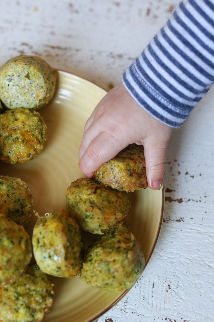 Baby's hand reaching for a mini broccoli and cheese egg bites. 
