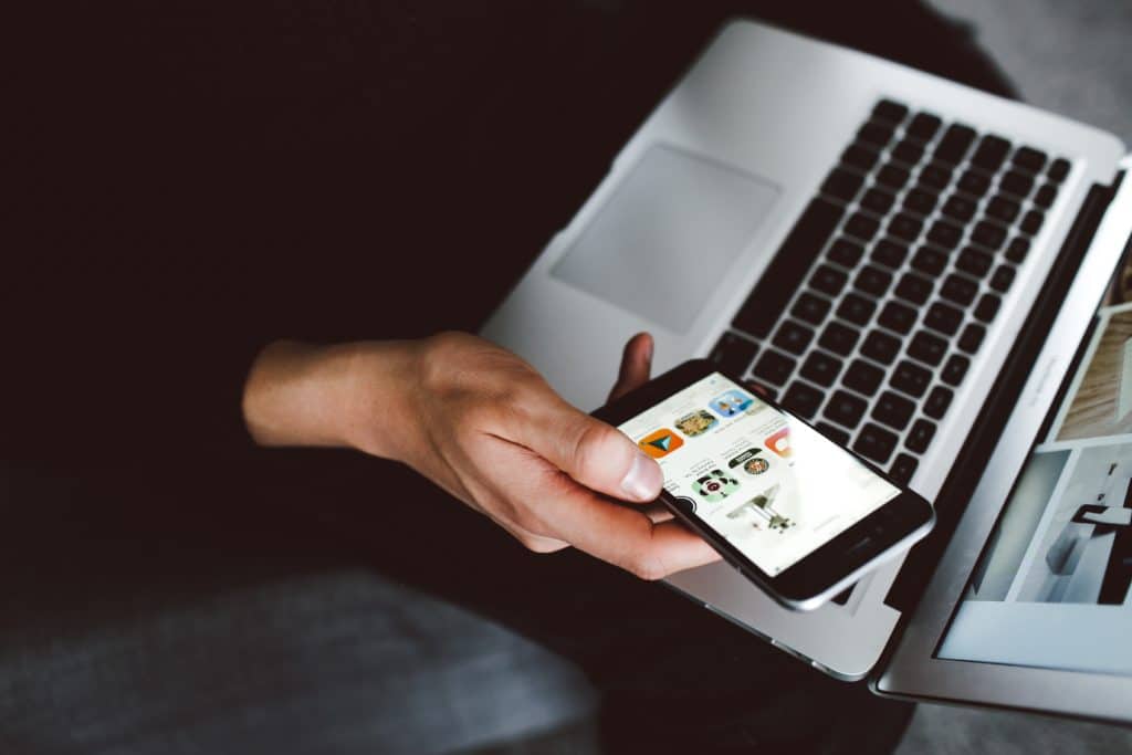 Hand holding a phone while on a laptop.