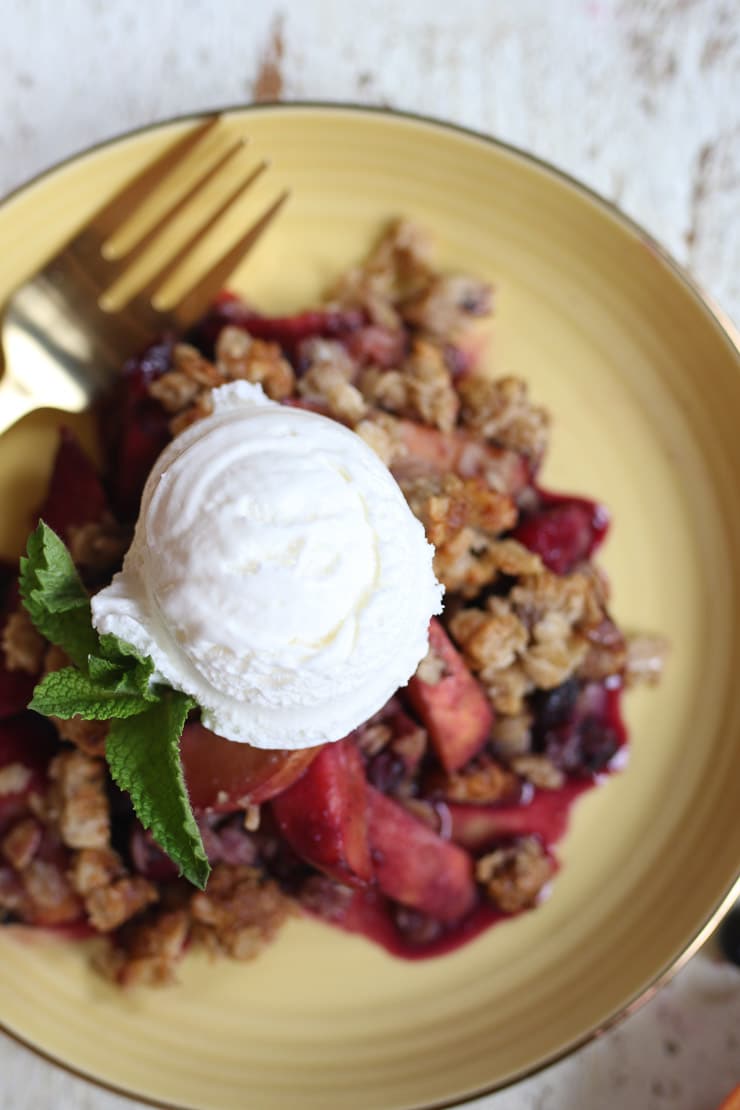 Blueberry and peach crisp on a yellow plate topped with ice cream.