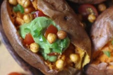 Guacamole and chickpeas stuffed sweet potato served on a wooden plate.