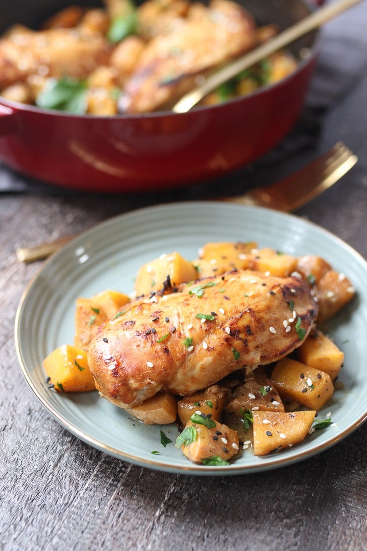 Persimmon and ginger chicken made in one pot served on a grey plate topped with seeds with a red pot containing additional chicken in the background