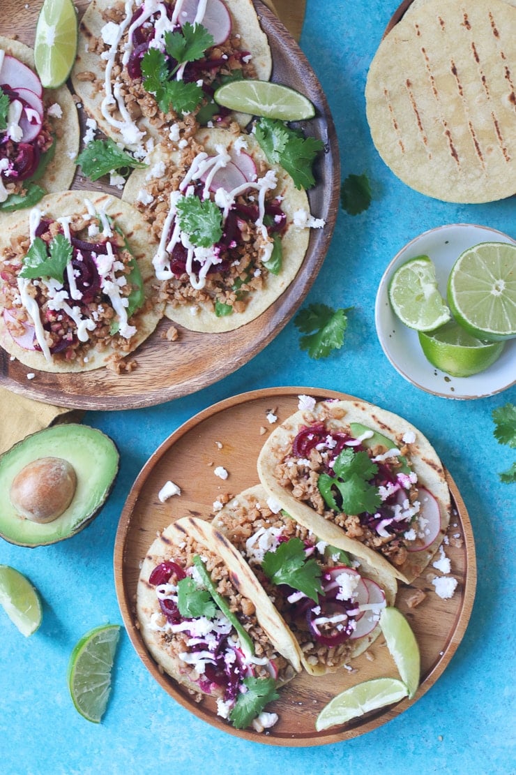 Birds eye view of multiple tacos on two wooden plates, filled with walnut taco meat and garnished with cilantro and pickled beets.