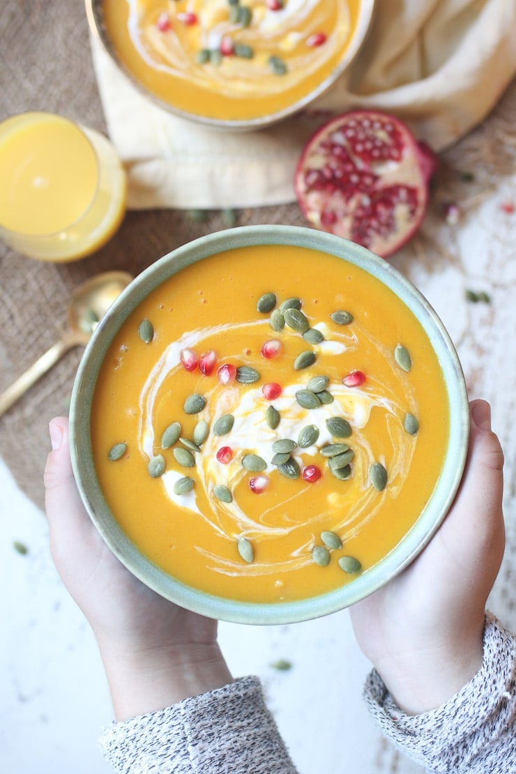 Orange soup served in a bowl garnished with pumpkin seeds and pomegranate seeds.