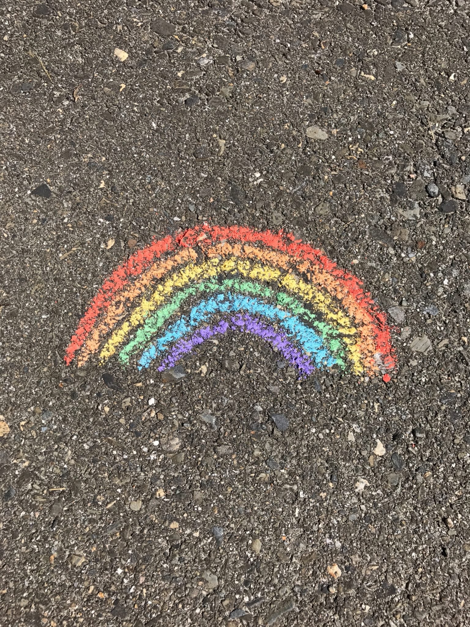A rainbow drawn with chalk on a sidewalk.