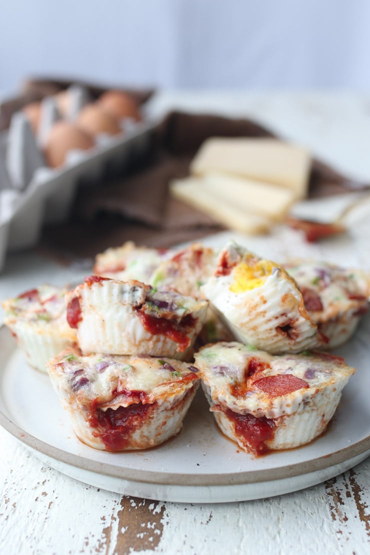 multiple keto and gluten free egg breakfast muffins stacked on top of each other on a white plate with a carton of eggs in the background