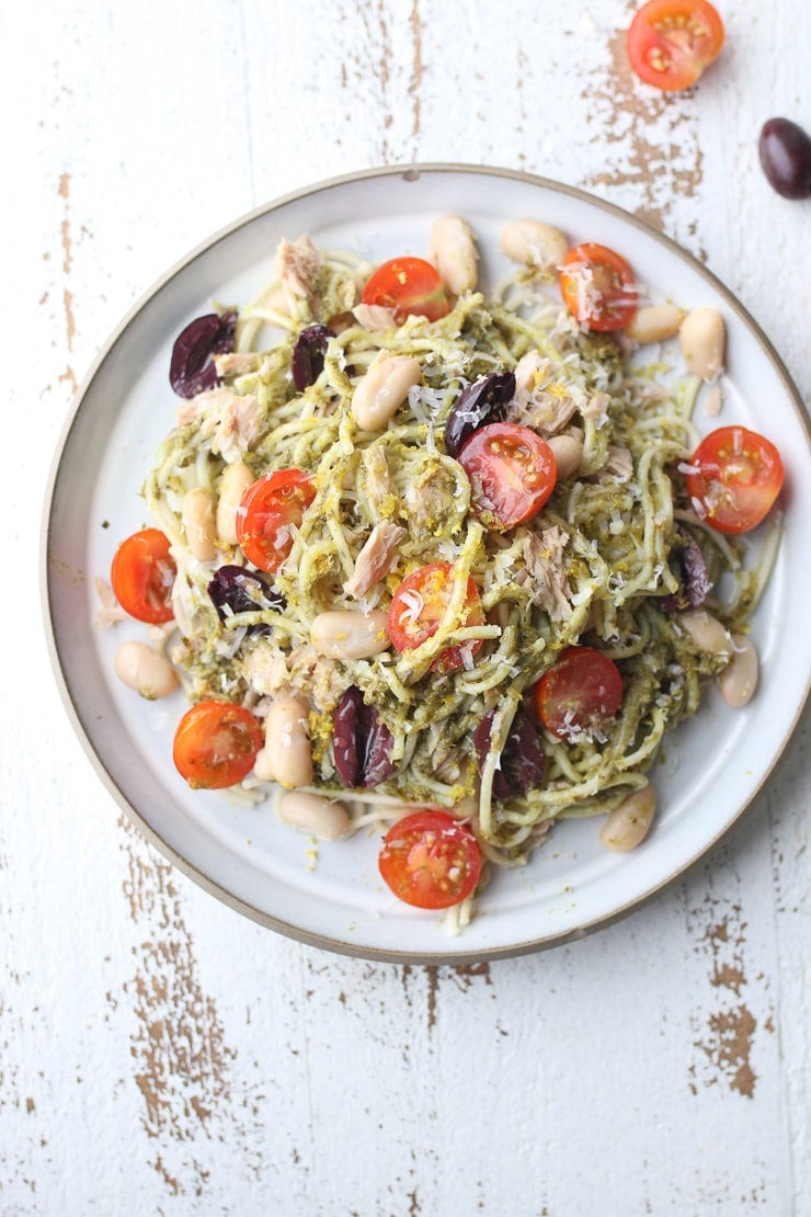 Birds eye view of tuna pesto pasta with topped with beans, tomato and olives.
