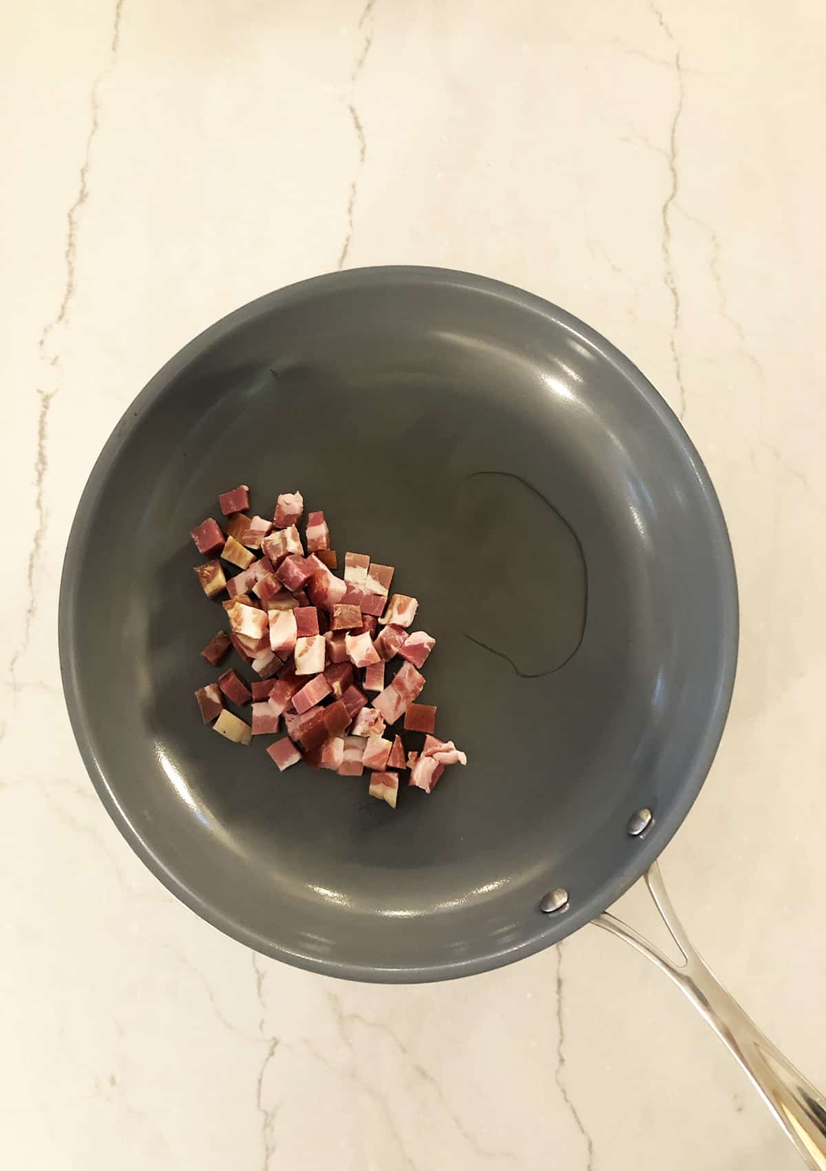 Pancetta cooking on a grey frying pan.