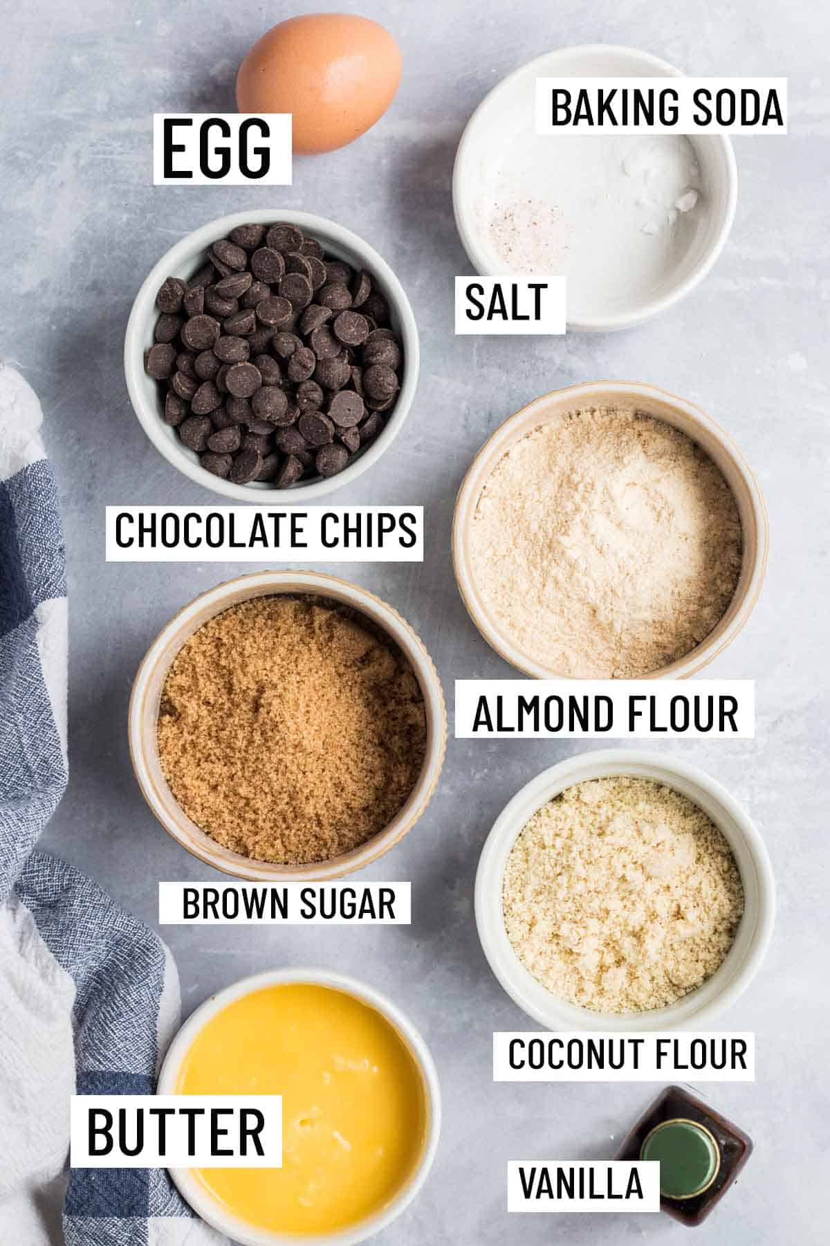 Birds eye view of portioned ingredients to make coconut flour cookies including flour, butter, vanilla, brown sugar, chocolate chips, salt, baking soda, and an egg.