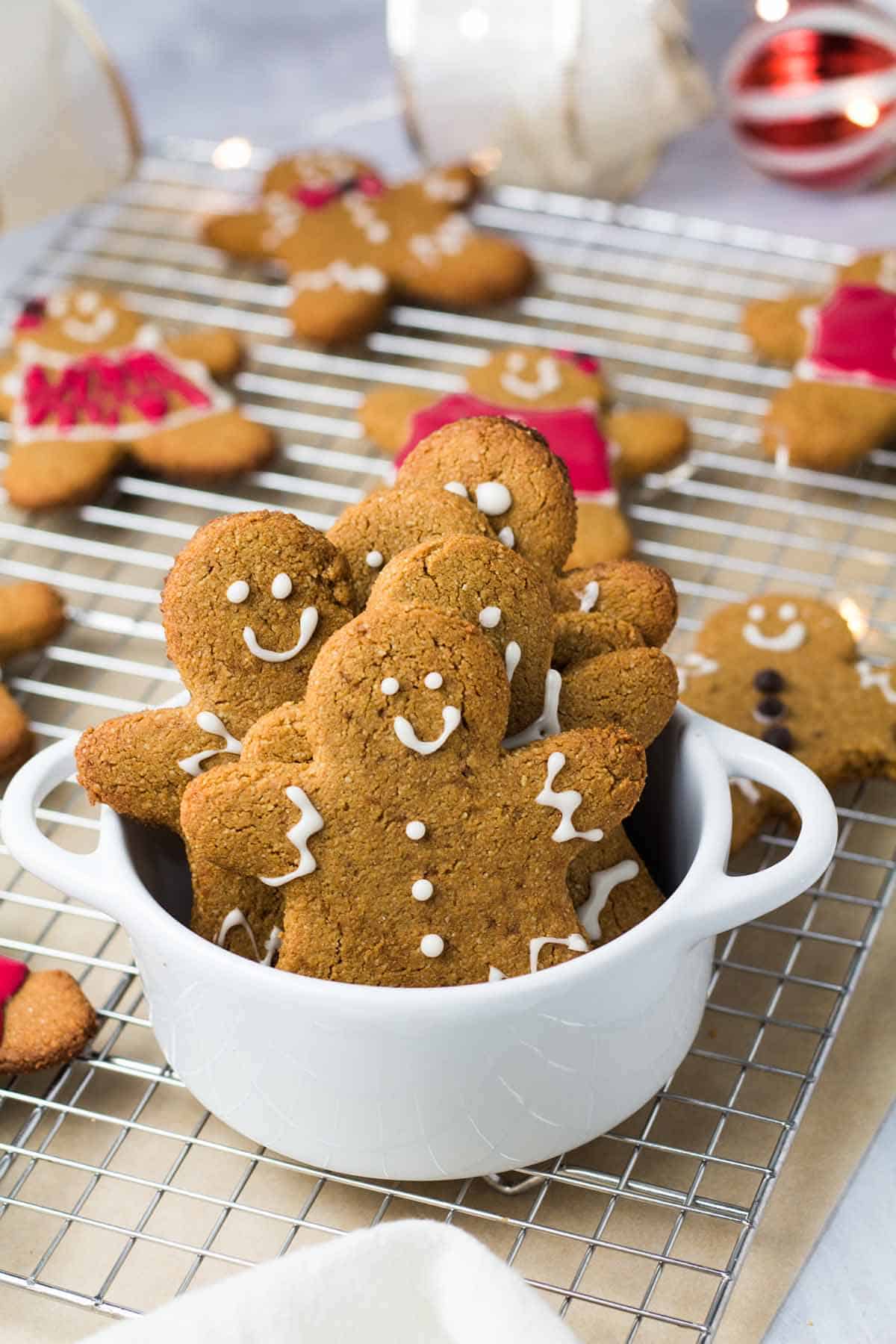 Several gingerbread cookies in a white bowl with more cookies on a baking tray in the background.