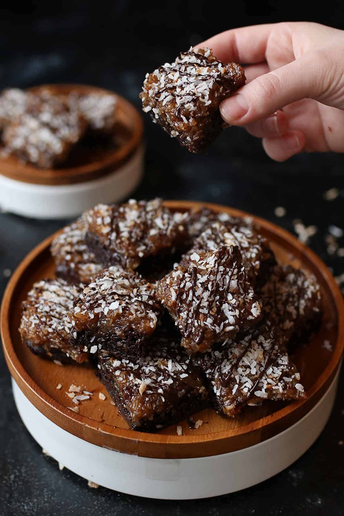 Hand picking up a brownie from a stack of brownies on a wooden plate. 