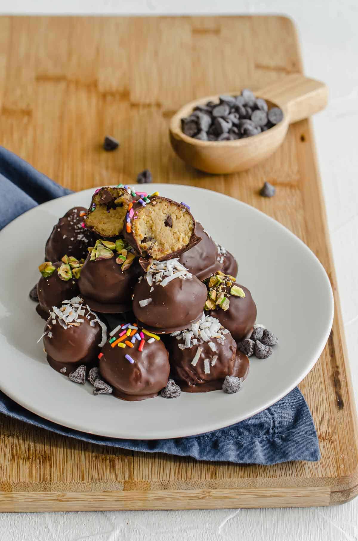 Close up of cookie dough balls on a white plate with chocolate chips in the background. 