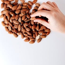 Hand reaching for one almond from a pile.