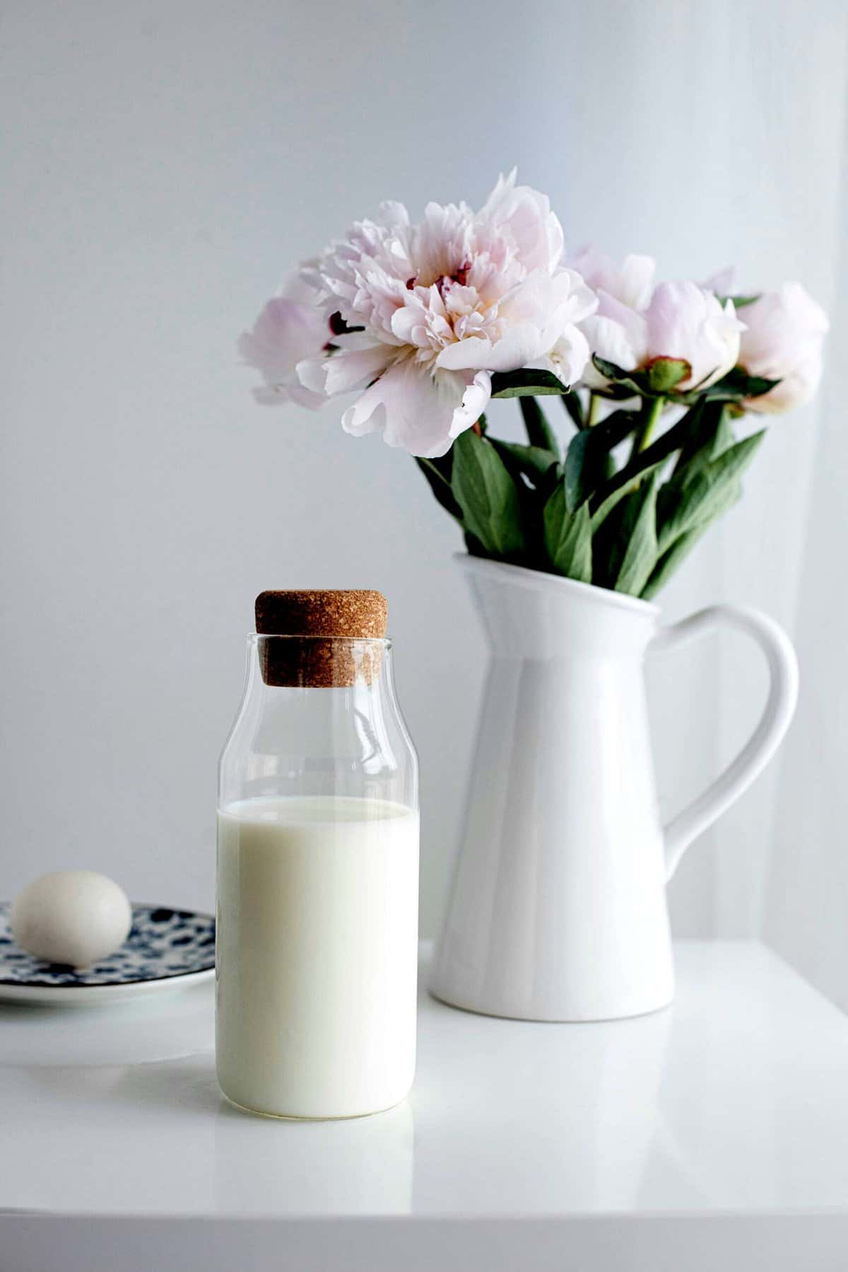 Glass jar of milk beside a vase of flowers.