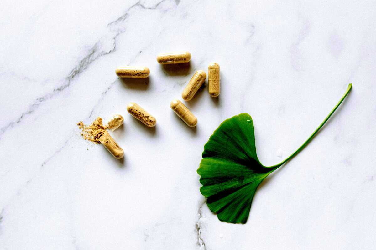 Dietary supplements and a green leaf on a marble table.